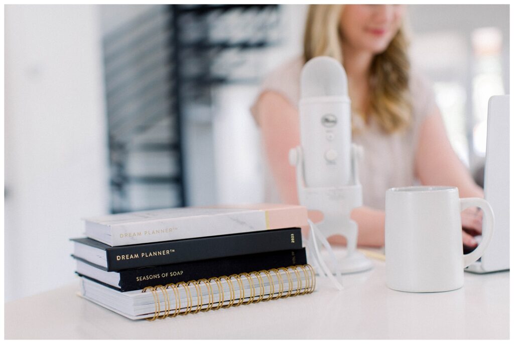 Close up shot of a stack of planners with a podcast microphone and a woman seated blurred in the background Denise Karis brand photography 