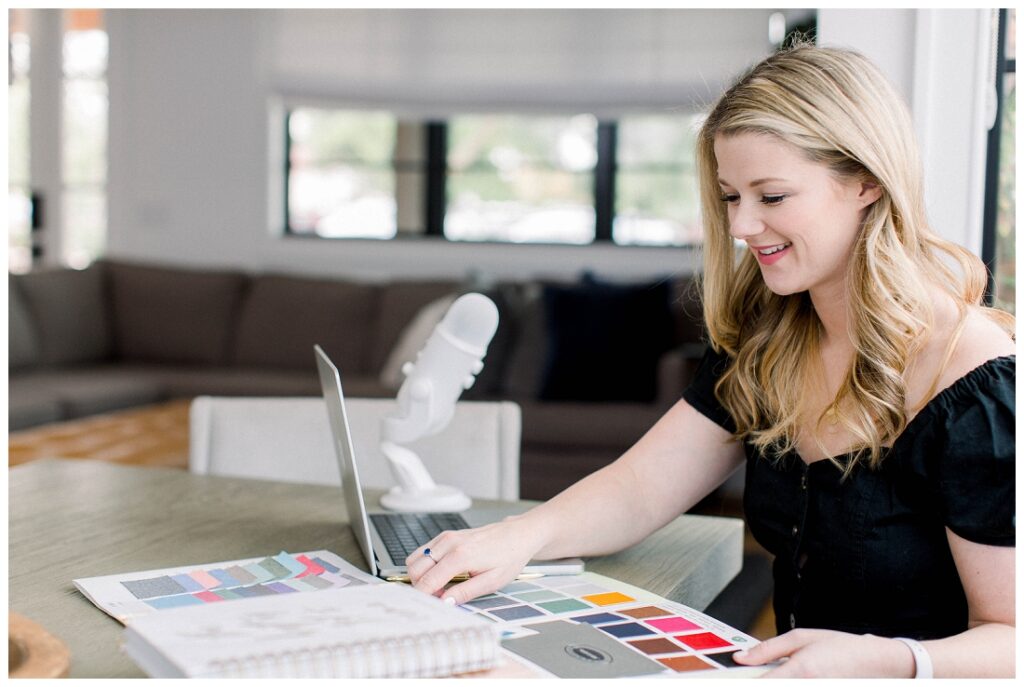 Denise Karis brand photography Woman on laptop with podcast microphone reviewing color swatches at a table. 