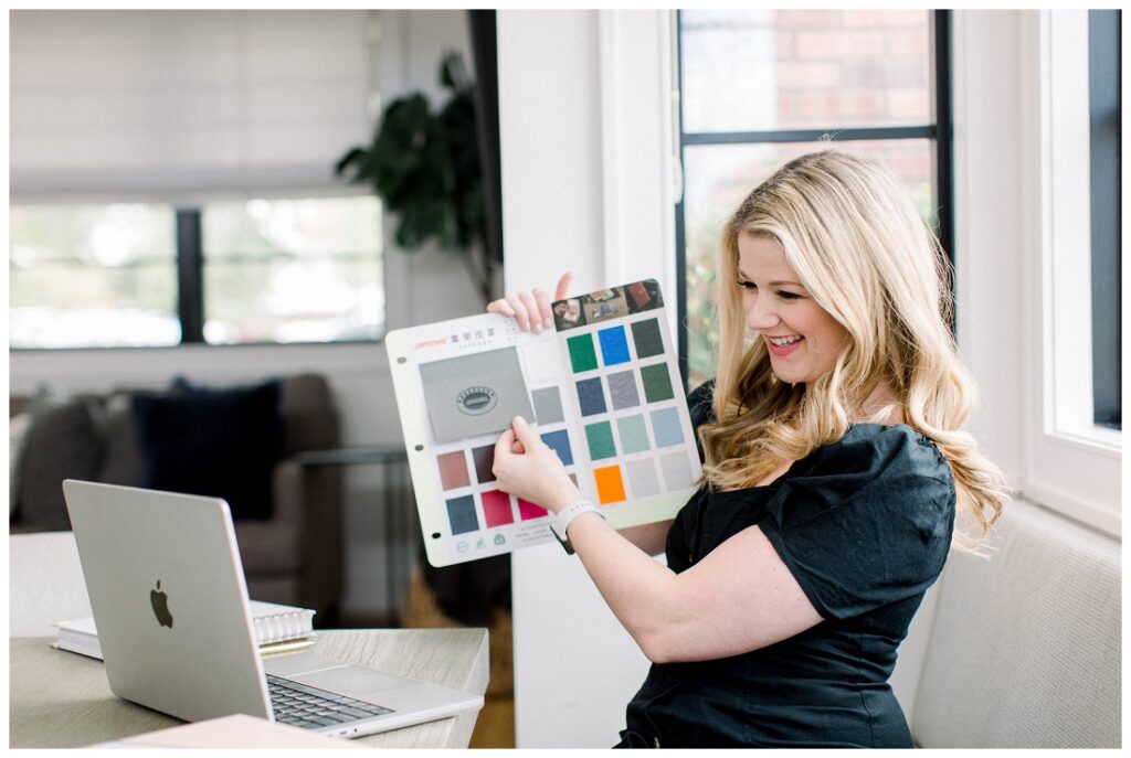 Denise Karis brand photography woman is "Live" on a laptop, she is holding a book of color swatches up to her laptop camera. 