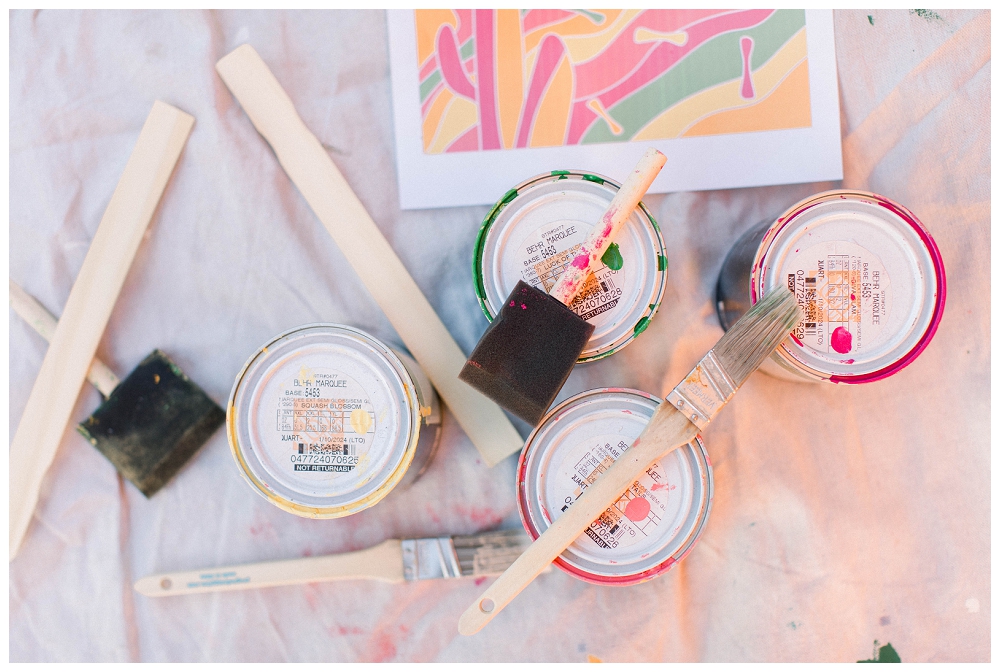 an image of paint supplies including paint, brushes, stirrers, and a drop cloth