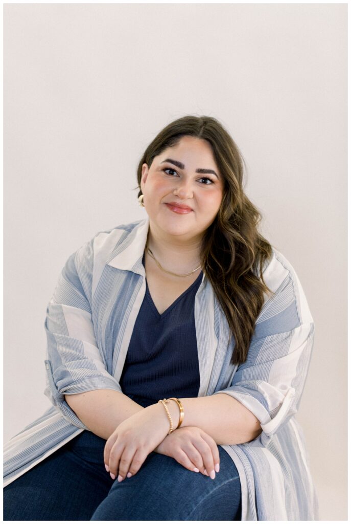 A headshot of a woman in a blue top in front of an off-white background. 