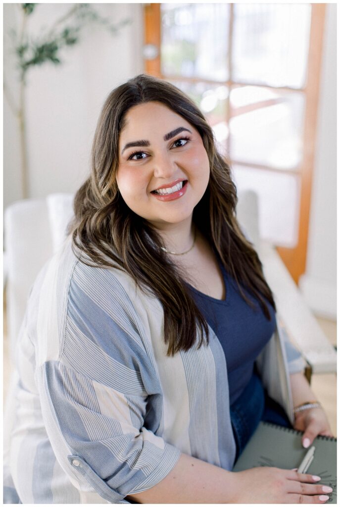a headshot of a woman in a blue top seated in a studio office space. 