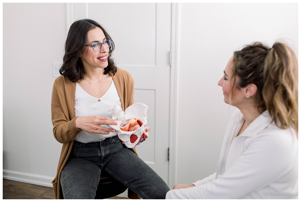 A physical therapist shows a model of a pelvis to a patient in a medical setting. 