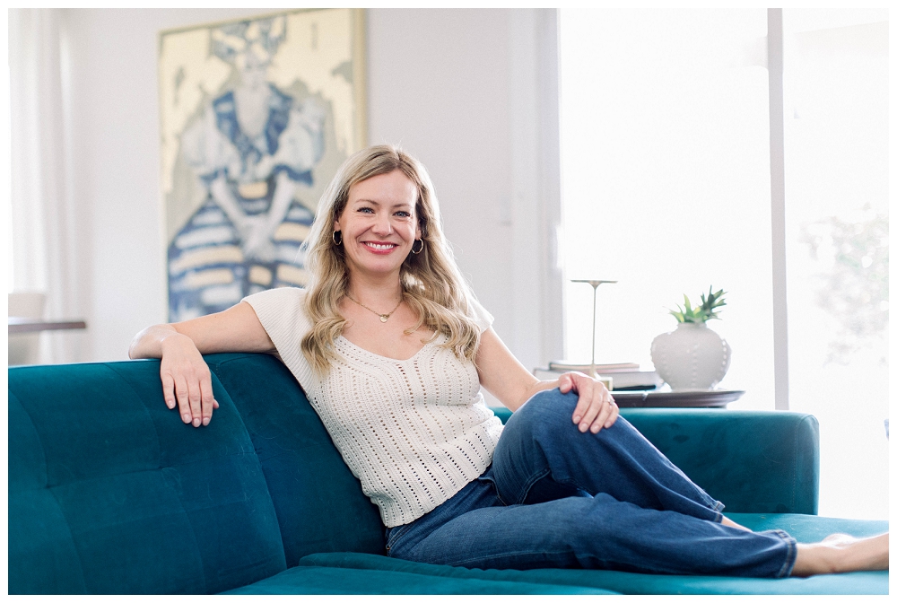 Branding portrait of a woman sitting on a sofa smiling at the camera. 