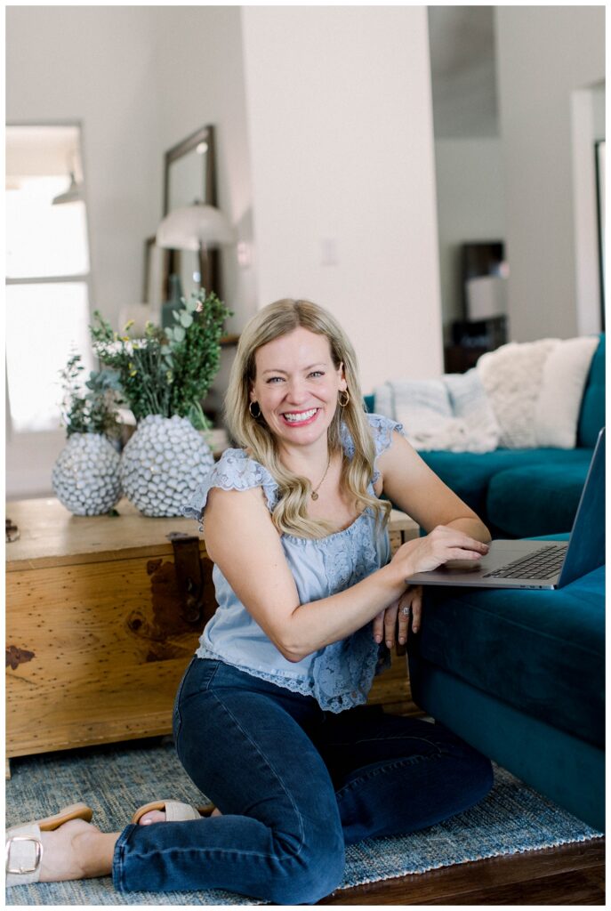 Branding portrait of a woman sitting on the floor with a laptop open on the sofa in front of her. 