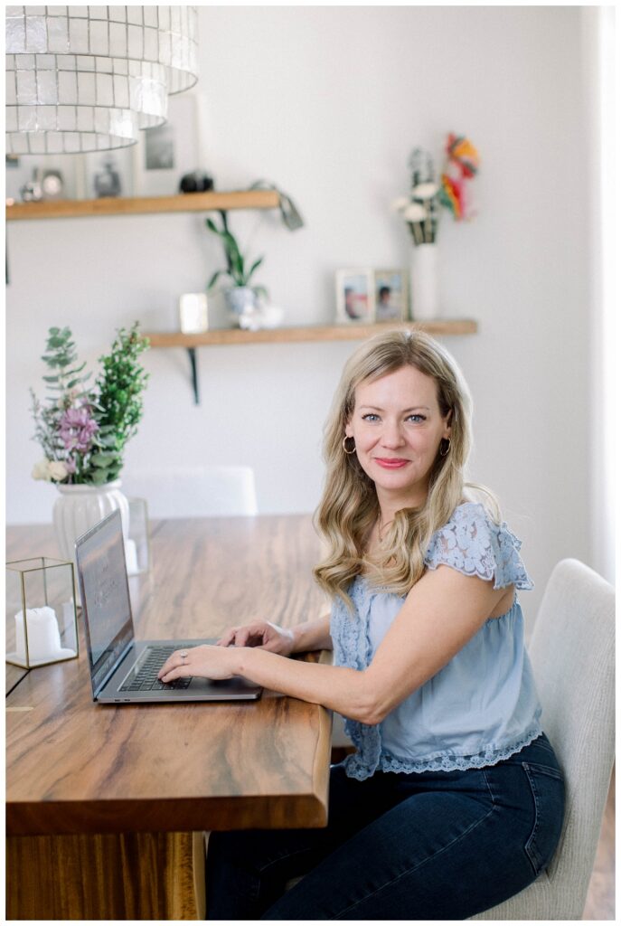 Branding portrait of a woman sitting at a table typing on a laptop. 