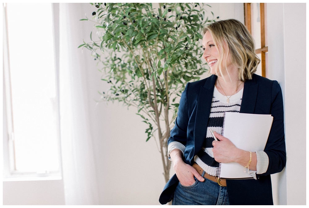 Headshot/branding photography. A woman laughs off to the side of the camera, she wears a navy blazer and holds a folder in her arm. 