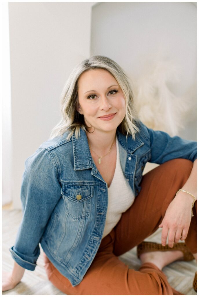 Brand photography/headshot photography. a woman in a denim blazer and orange pants poses in a living room setting. 