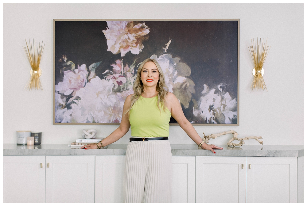 A woman in a bright green top stands in front of a floral painting. 