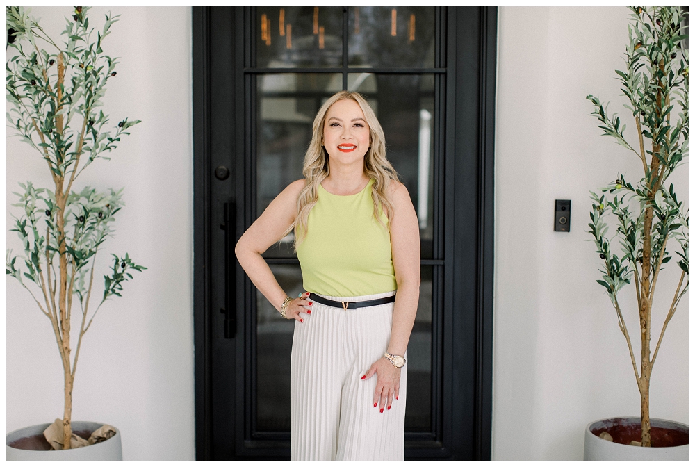 A woman in a neon yellow top stands in front of a black front door. 
