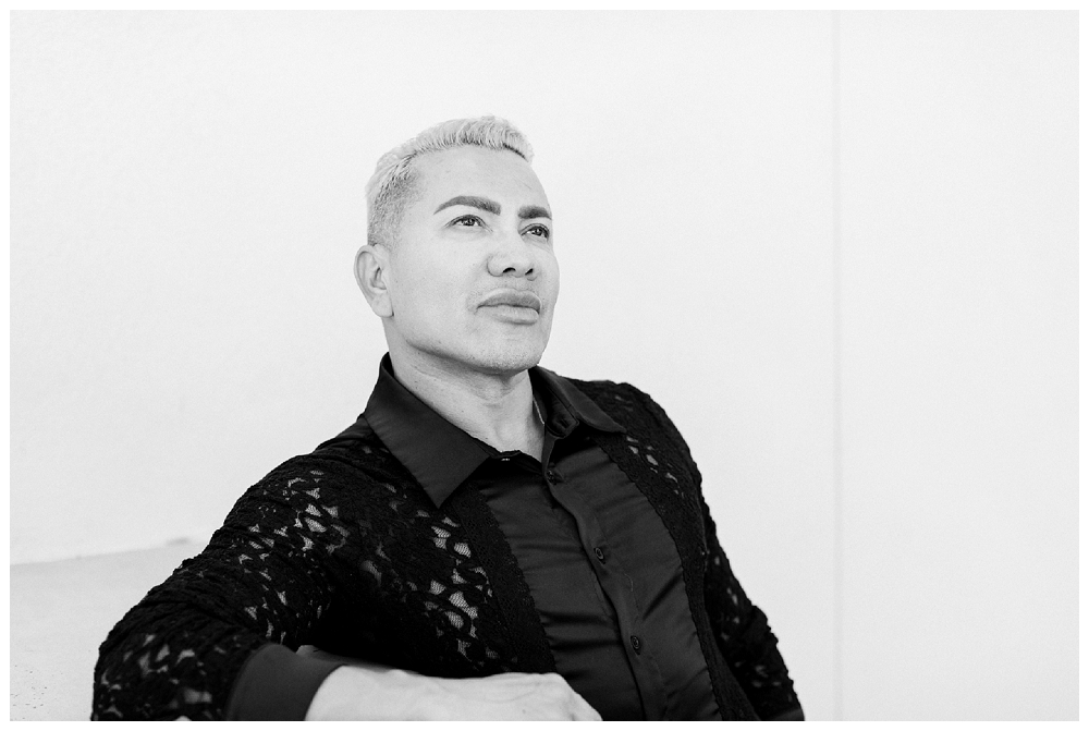 A black and white image of a man wearing a black collared shirt looks upwards. 