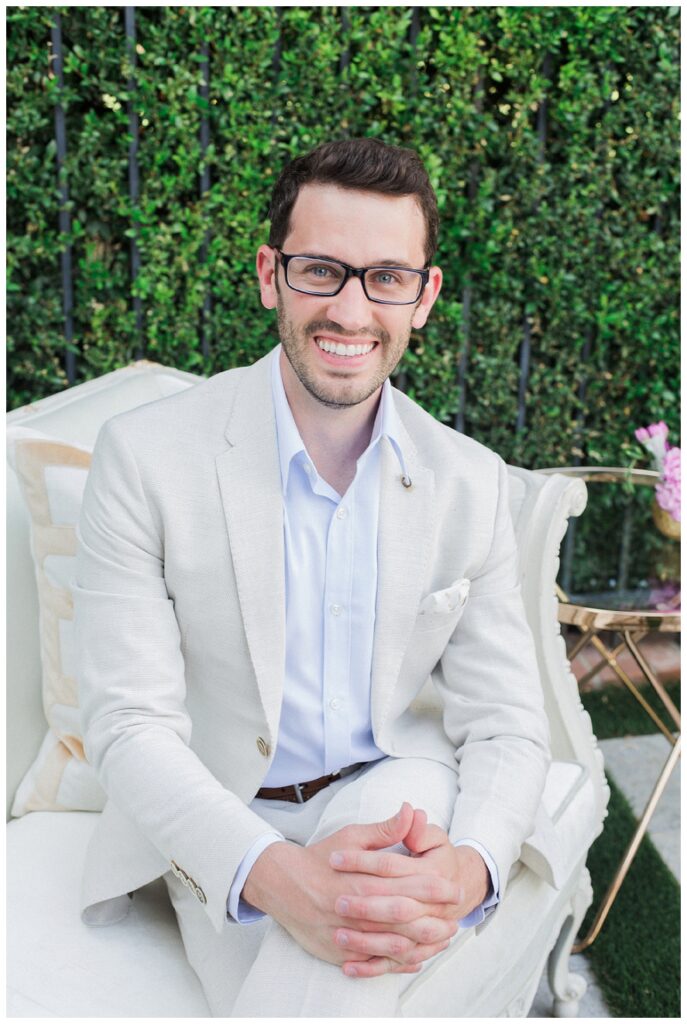 A headshot of a well dressed man wearing a light suit and glasses.