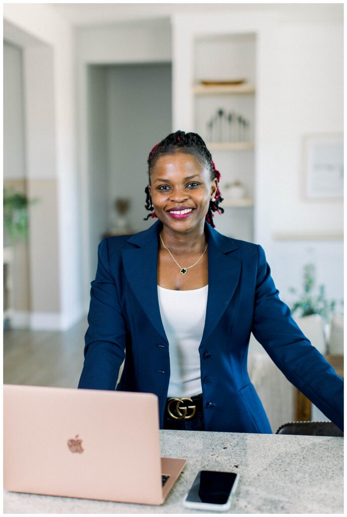 Arizona Branding Photography A woman in a navy blazer stands in a home, a laptop is open on the counter in front of her. She smiles at the camera. 