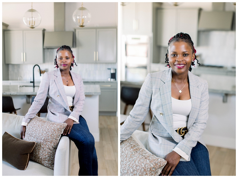A womain in a grey blazer sits on the arm of a sofa and smiles at the camera. 