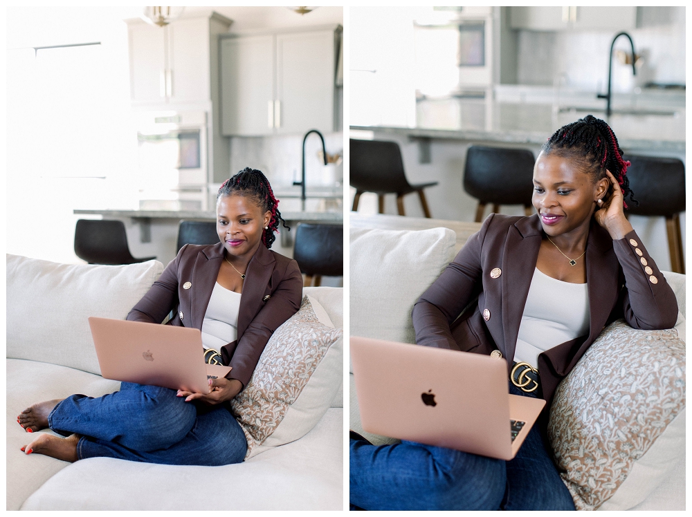 A womain in a brown blazer and jeans sits on a sofa with a laptop open in her lap. 