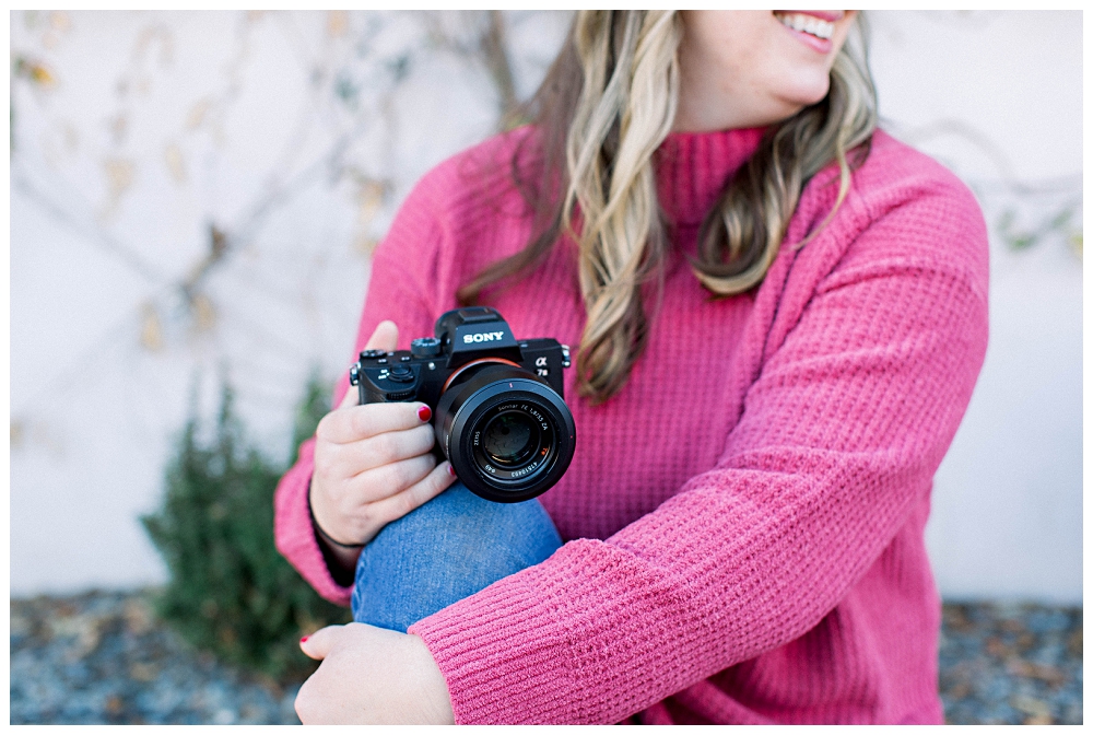 Branding portrait a woman in a pink top holds a camera. 