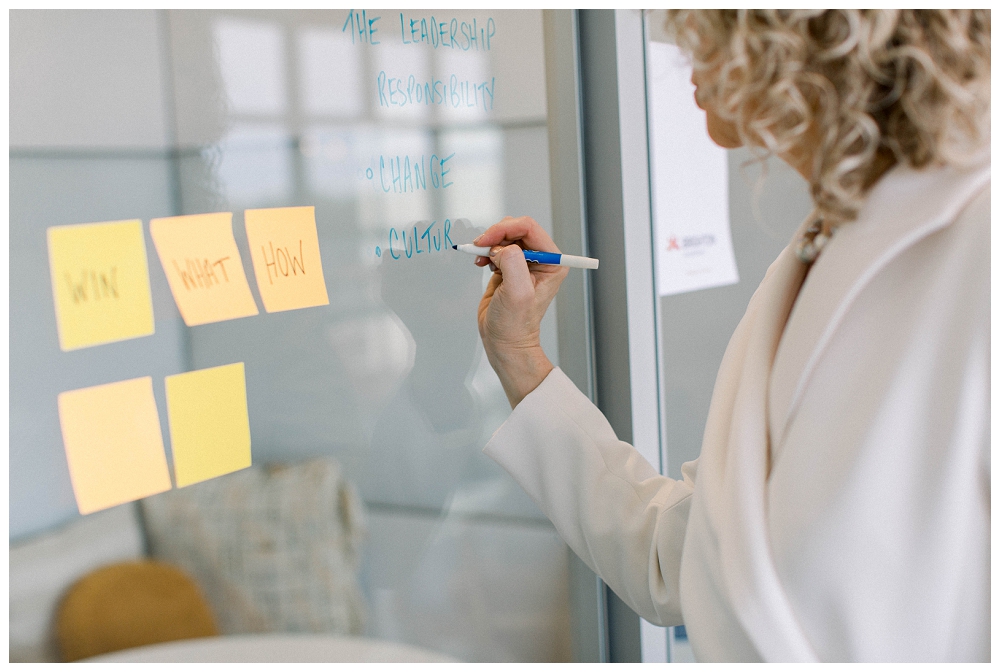 a woman writes on post-it notes that are stuck on a glass wall. 