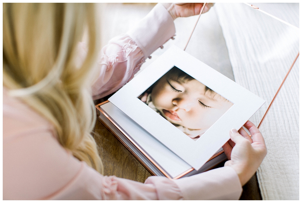 over the shoulder, a woman looks at photos of a newborn baby that have been printed and put in a beautiful box