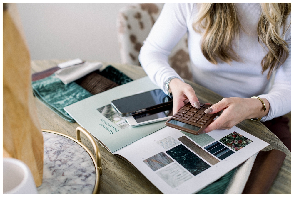 Branding portrait a woman punches numbers on a calculator, there are design books open on the table. 