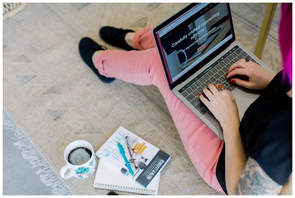 Branding portrait a woman sits on the floor working with a laptop open on her lap. 