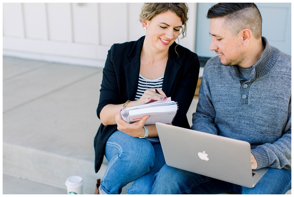 Branding Portrait a man and woman work together, he is on a laptop, she holds a notebook, they are talking. 
