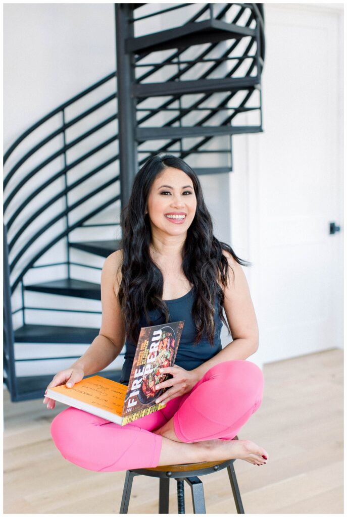Branding Portrait a woman holds a cookbook while seated on a stool. 