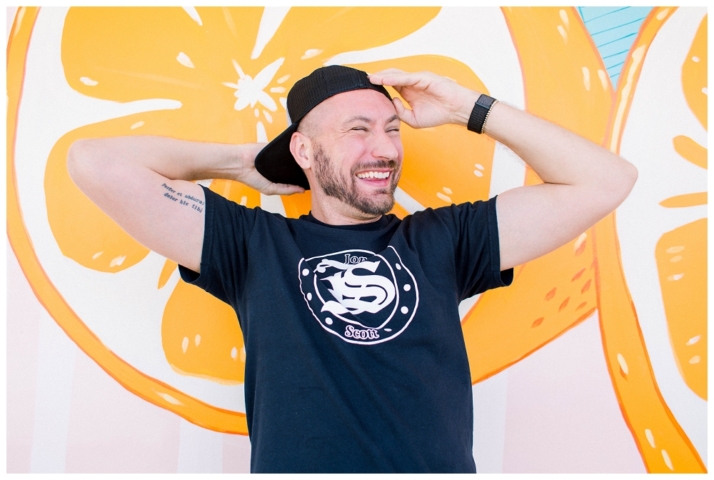 Branding Portrait a man in a hat stands smiling against a citrus mural. 