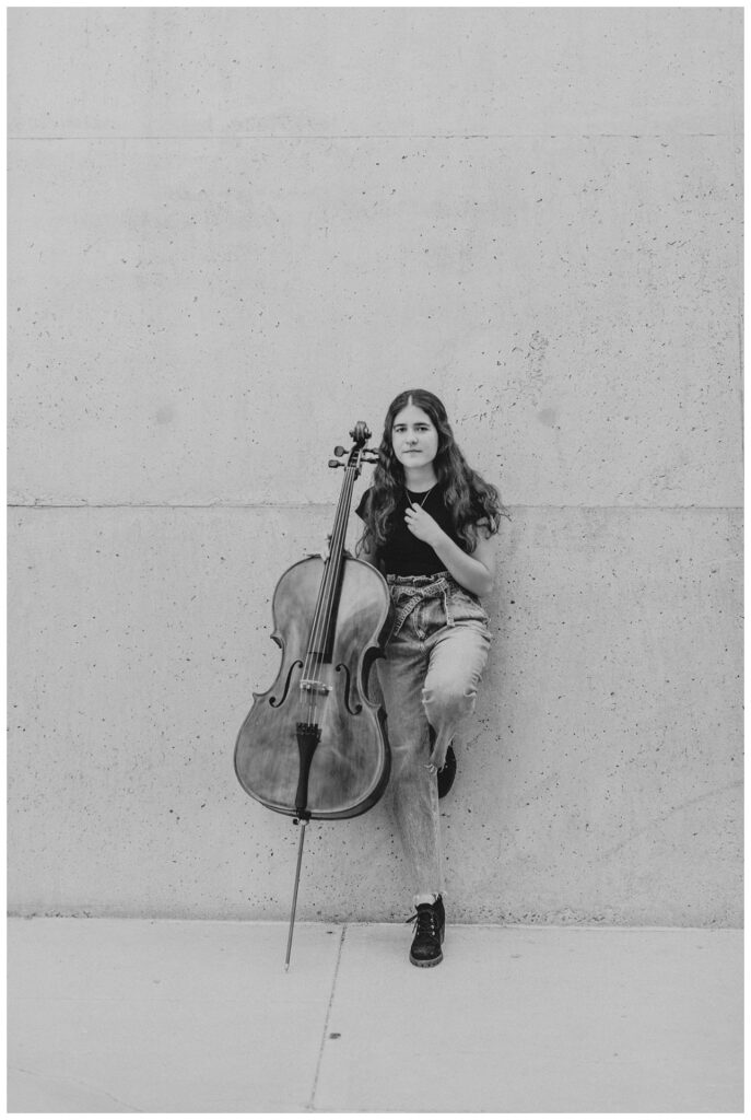 Branding Portrait a cellist stands against a concrete wall. Image is in black and white. 