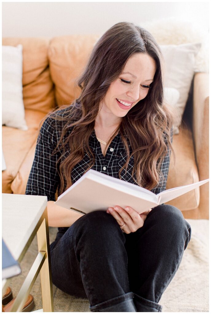A woman reads a notebook while sitting in front of a sofa. 