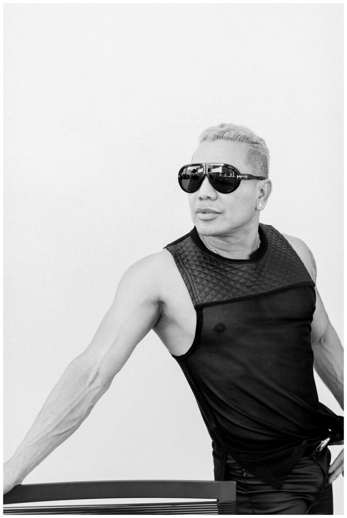 Branding Portrait a man wears a black mesh tank top and sunglasses. The imagge is black and white. He looks off camera unsmiling. 