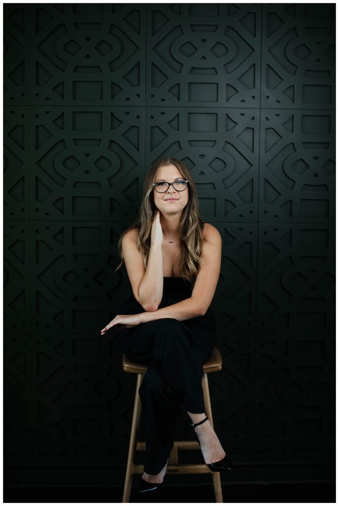 Branding Portrait a woman sits on a stool in front of a black wall. 