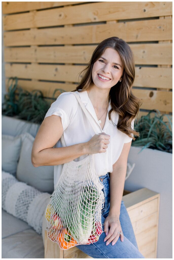 Branding Portrait a woman smiels at the camera, she holds a bag of produce. 