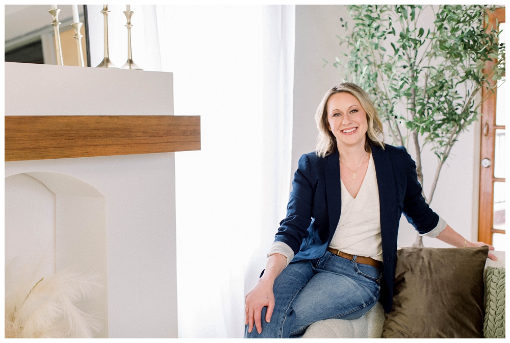 Branding Portrait a woman smiles at the camera while sitting on a sofa arm. 